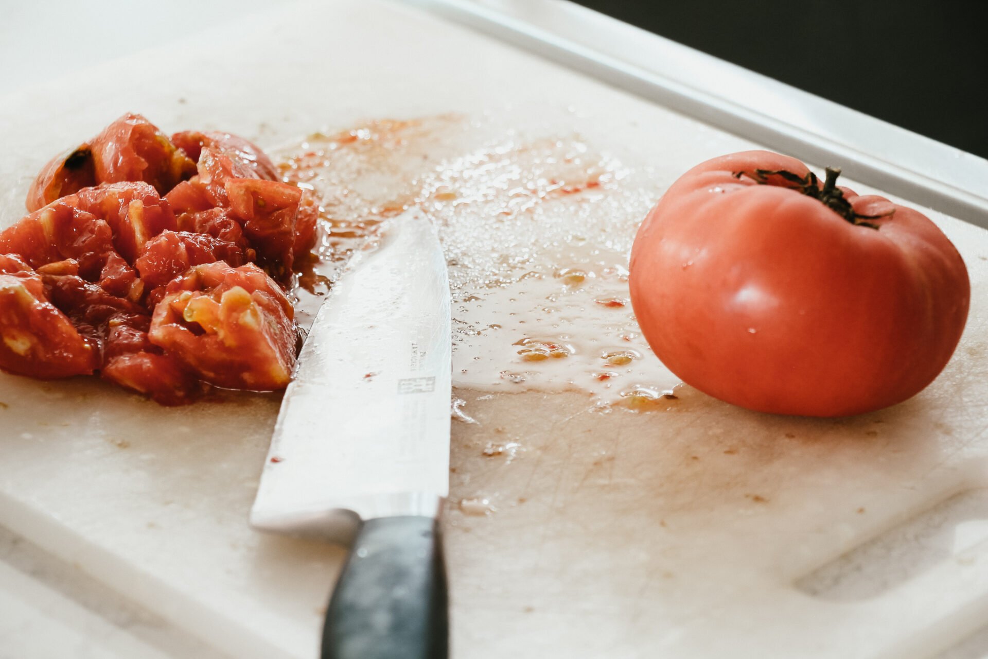 a white plastic cutting board with a knife cutting up tomatoes to make marinara sauce 
