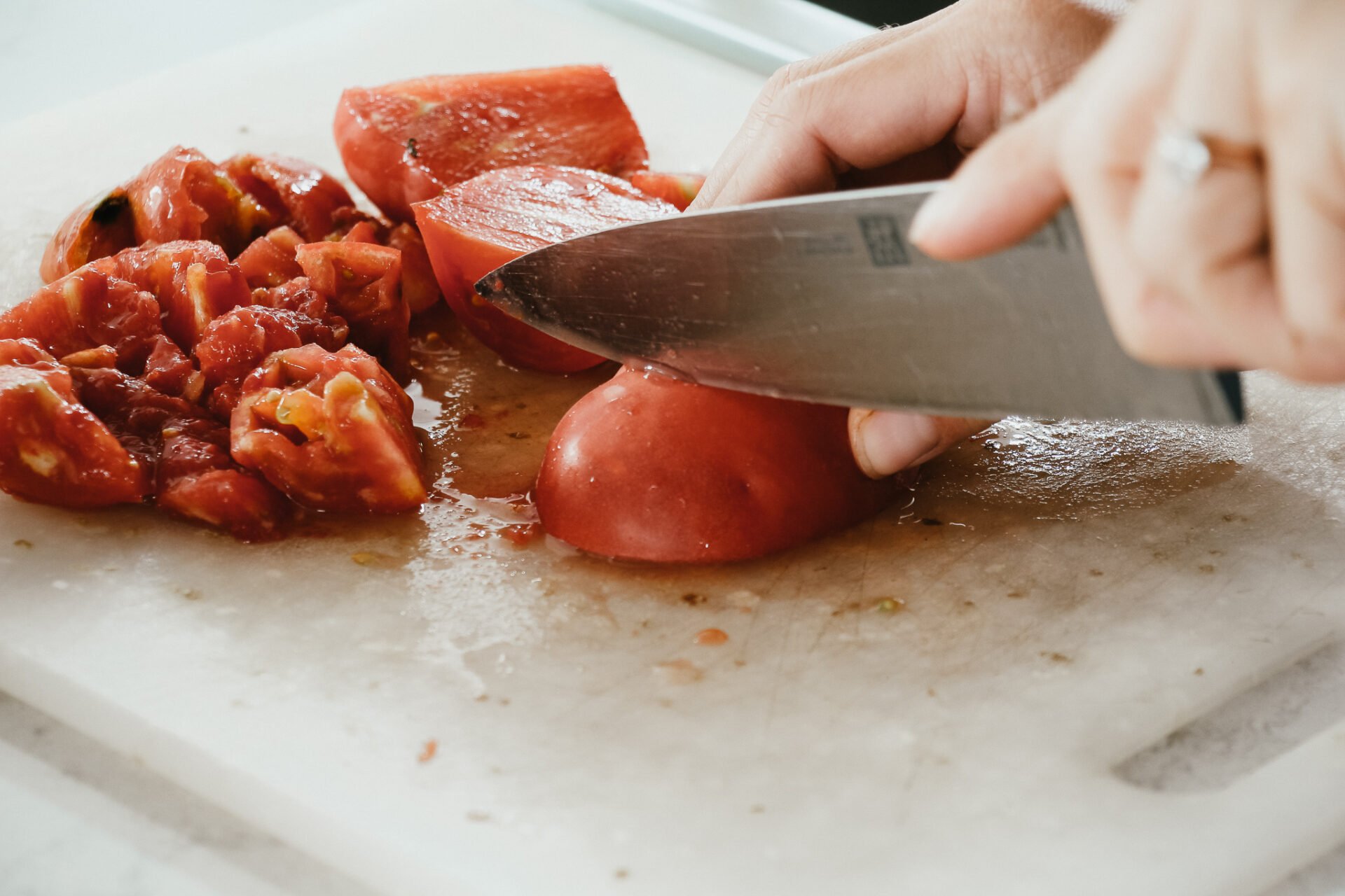 a woman cutting up tomatoes on a white cutting board