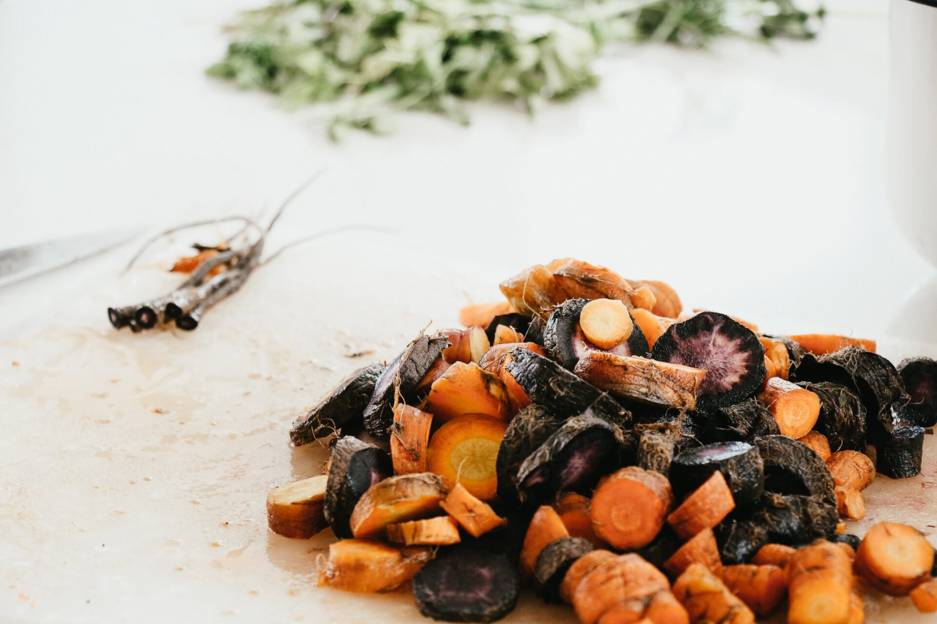 orange and purple carrots on a cutting board on a white marble countertop