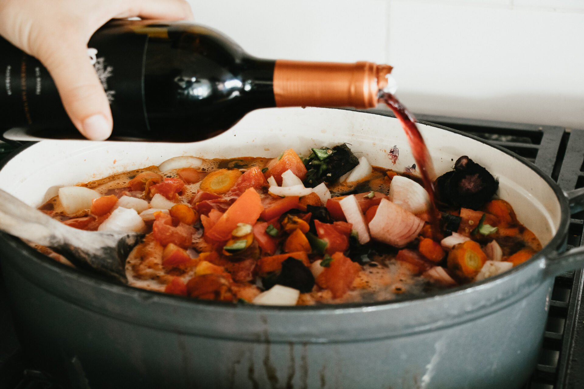 pouring red wine into the blue dutch oven over the gas cook stove