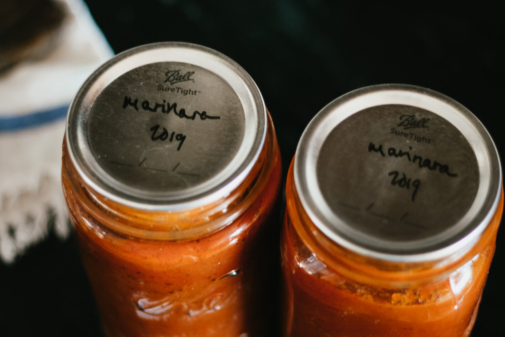 two jars filled with red marinara sauce with a metal canning lid on top on a black counter top