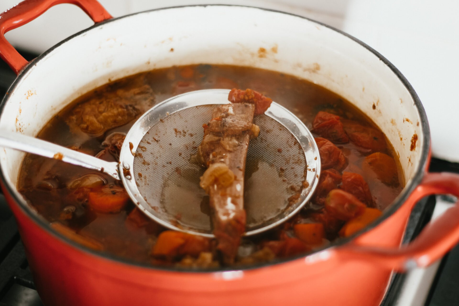 beef bones strained from a sauce on the stove in a red dutch oven 