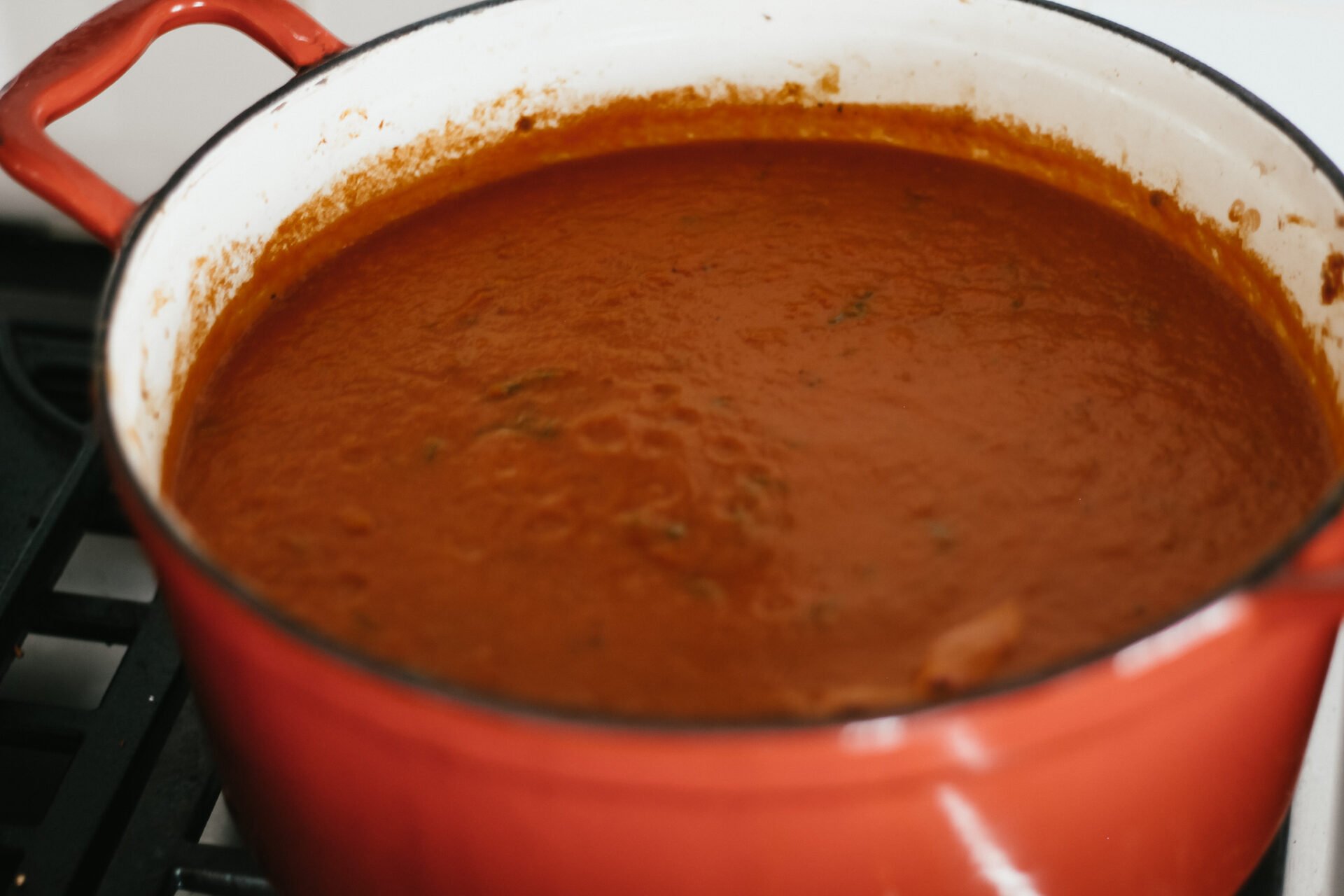 marinara sauce simmering in a red dutch oven over the gas stove