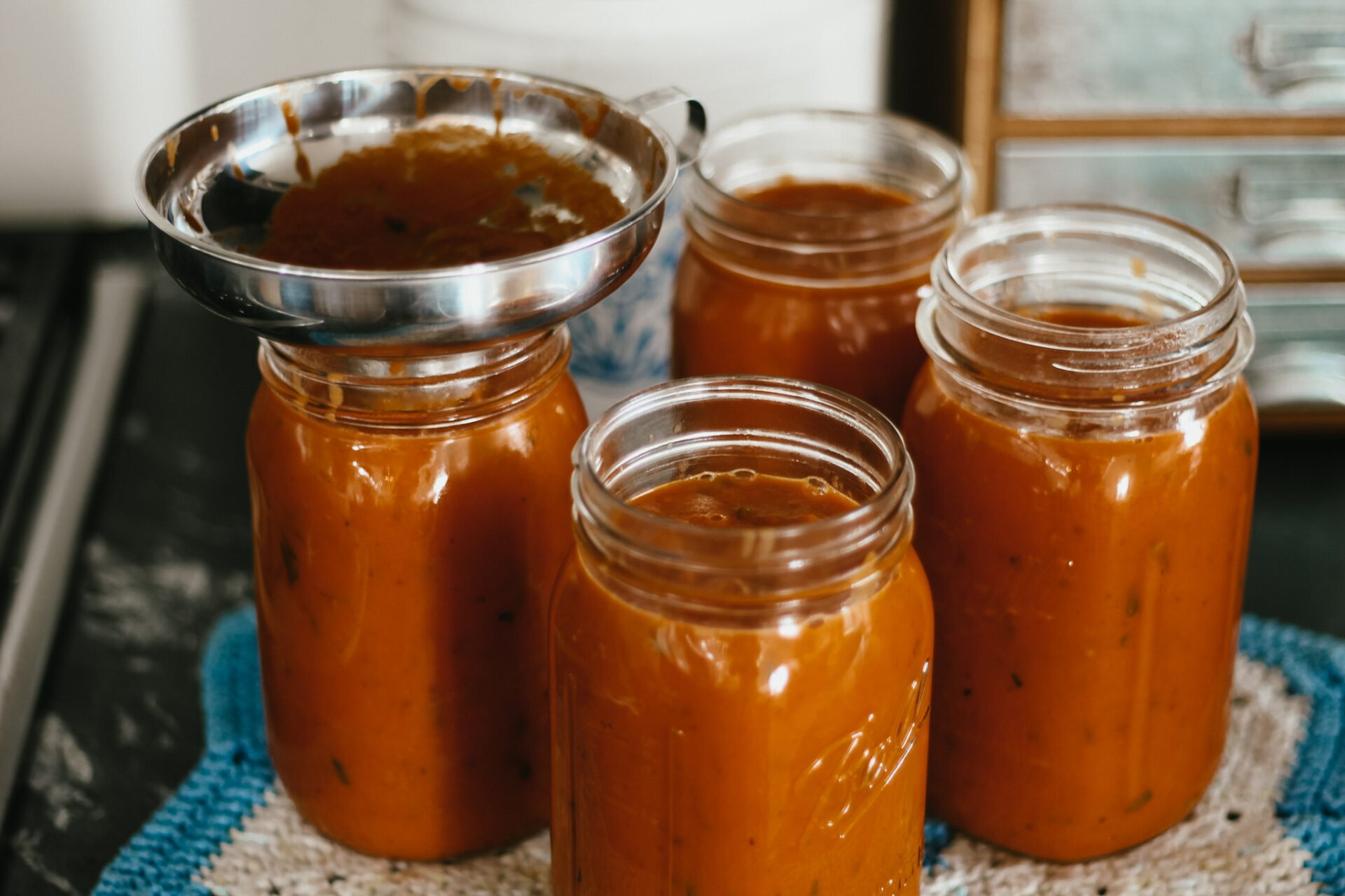 stainless funnel in a glass jar funneling marinara sauce into the canning jars