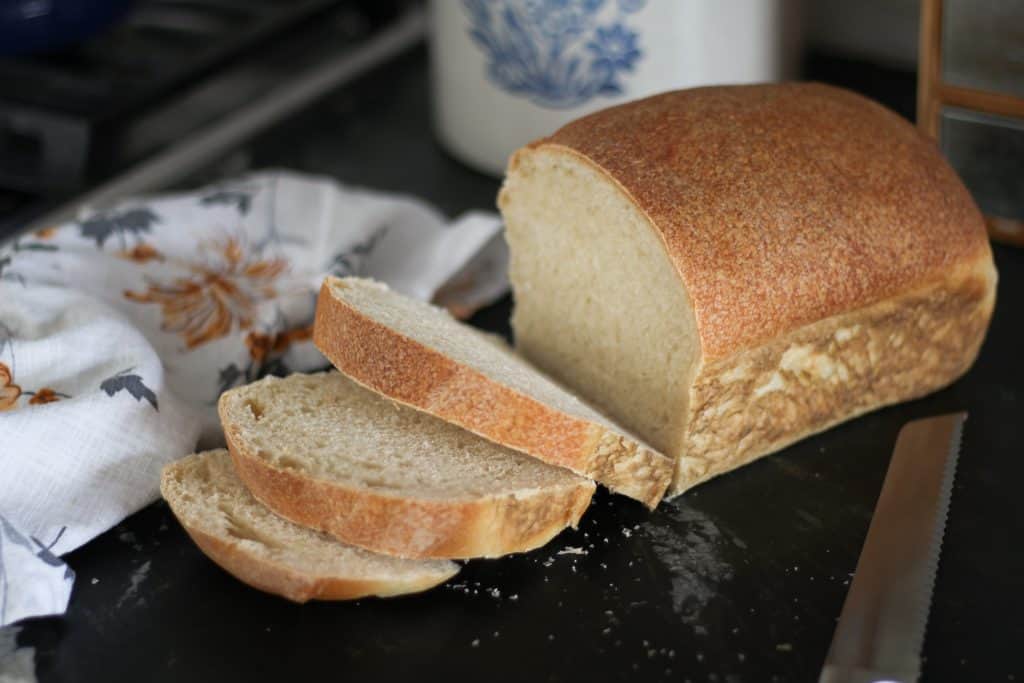 golden brown loaf of sourdough sandwich bread with a fews slices cut.