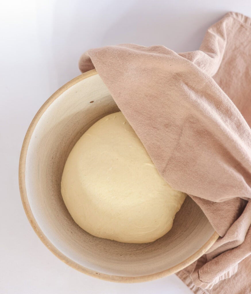 covering cinnamon roll dough in greased bowl with towel for bulk ferment.