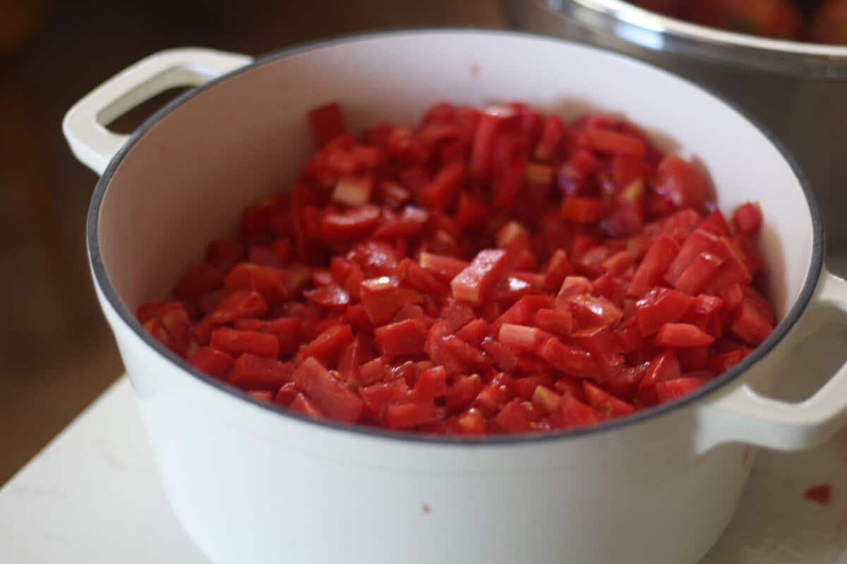chopped red tomatoes in a white dutch oven on a marble countertop