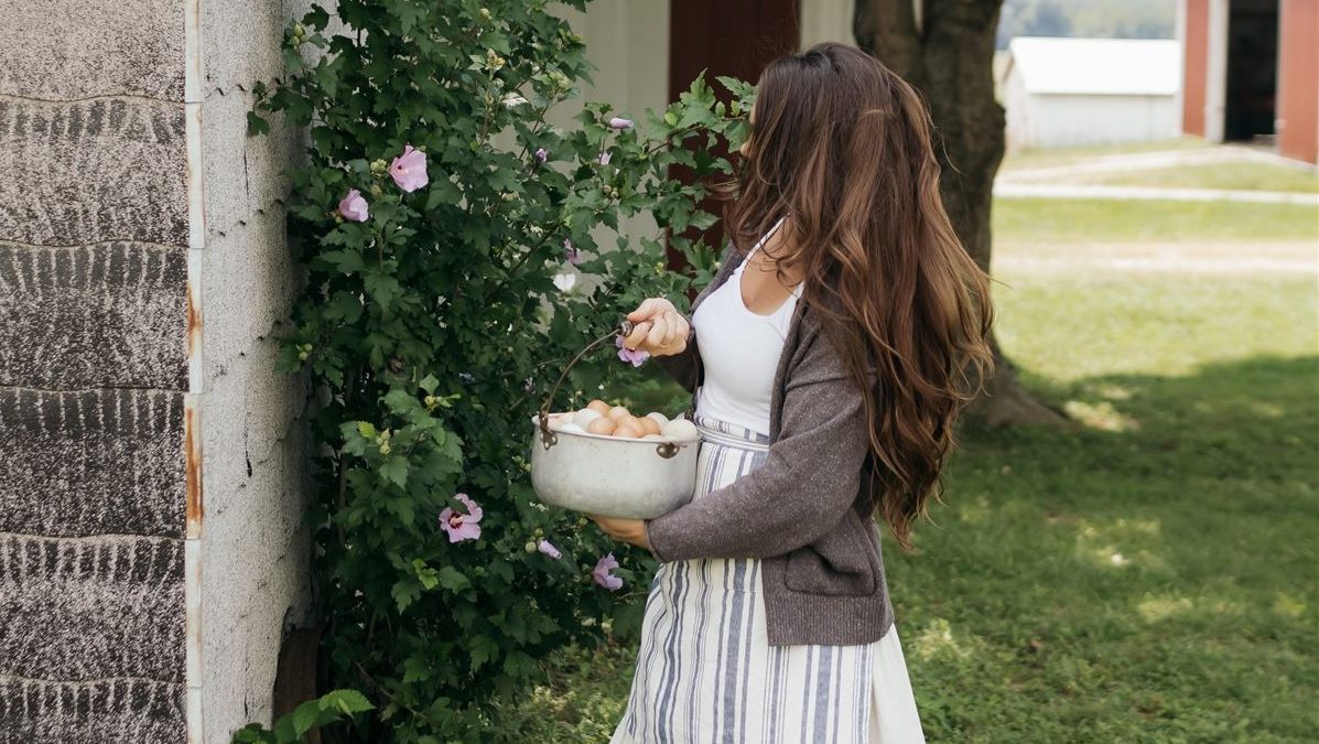 woman with long hair gathering eggs in a dress and apron