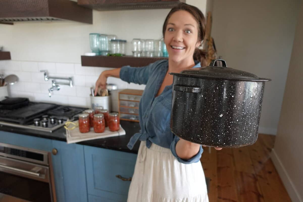 woman holding an enamel water bath canner in front of her blue kitchen cabinets