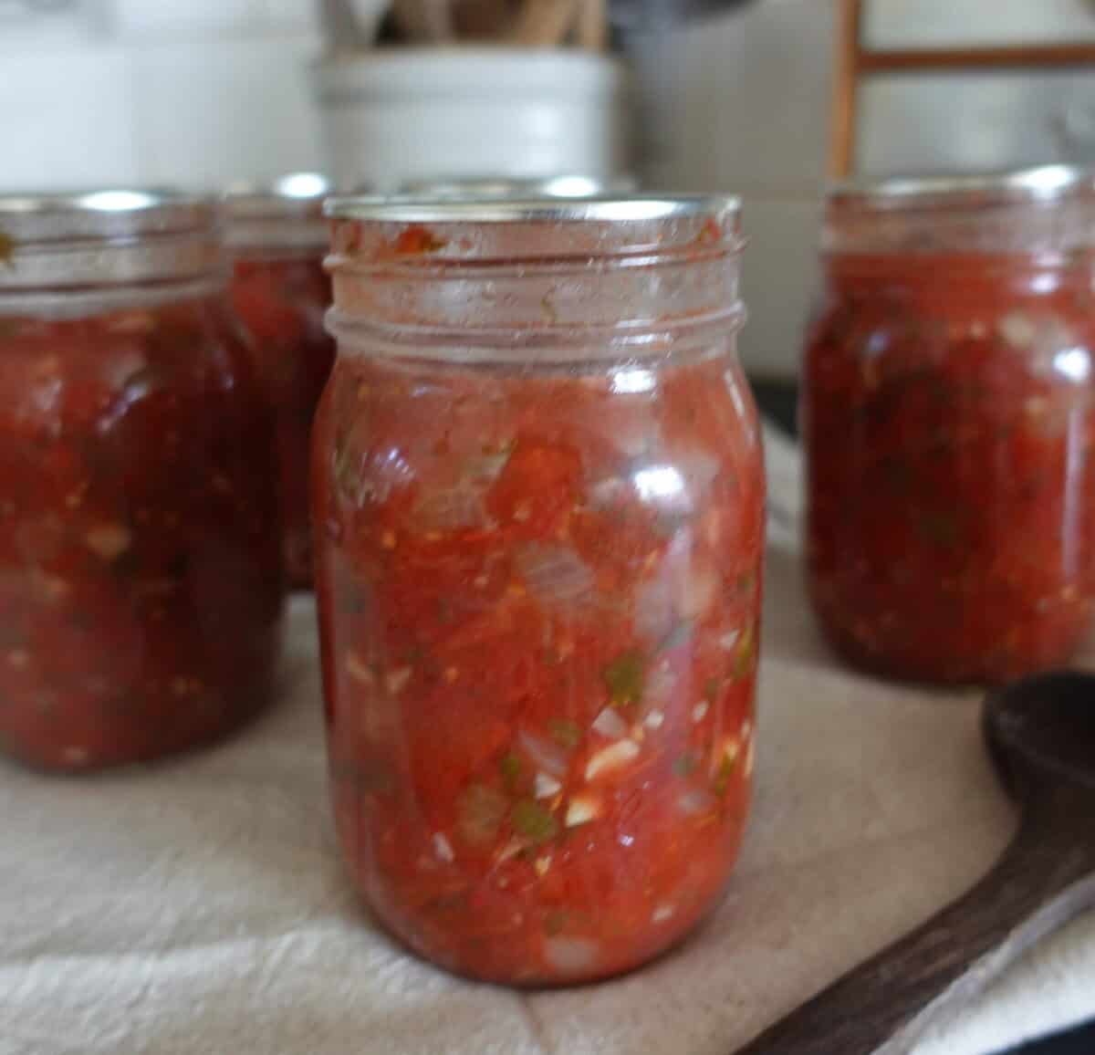 multiple jars of chunky salsa with peppers, onions, and tomatoes on a white tea towel