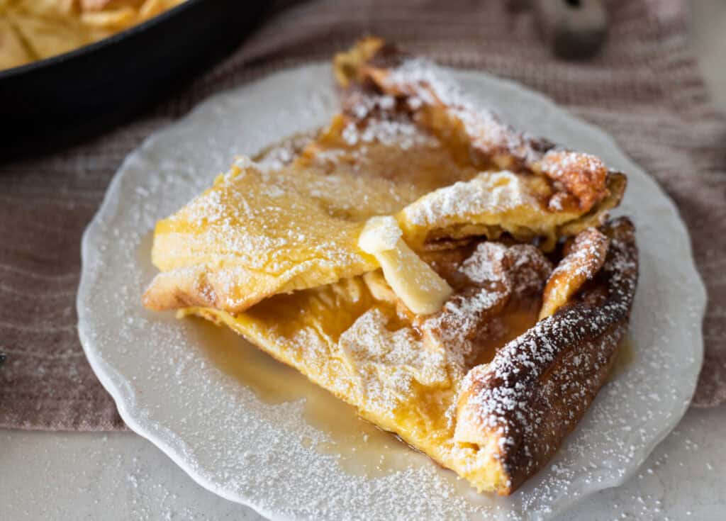 dutch baby pancake with melted butter, maple syrup, and powdered sugar