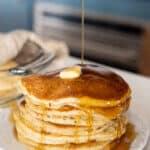 stack of fluffy sourdough pancakes with butter and syrup poured over.