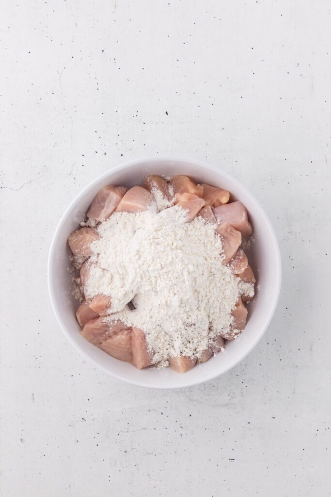 tossing raw chicken pieces in flour breading