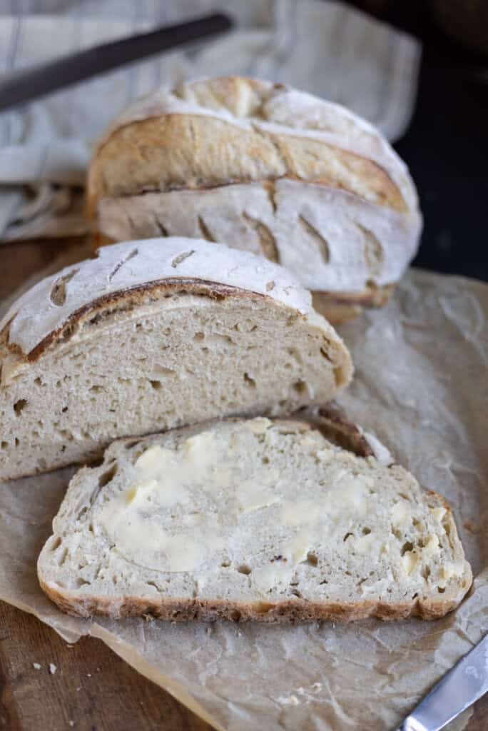sourdough artisan loaf sliced in half with a buttered slice.