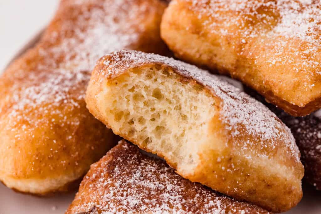 sourdough beignet with a bite against other beignets in the background.