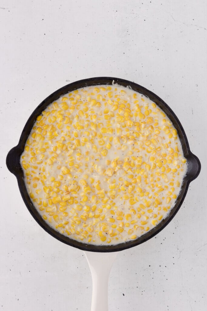 Creamed corn simmering in a black cast iron skillet with a white handle.