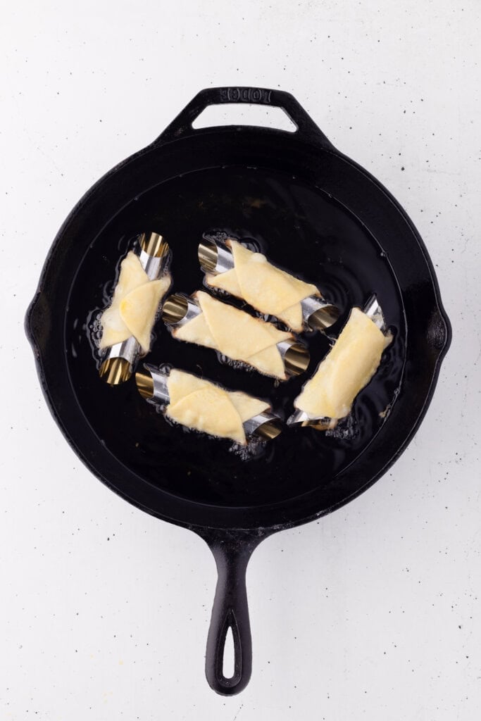 frying sourdough cannoli on forms in cast iron skillet.