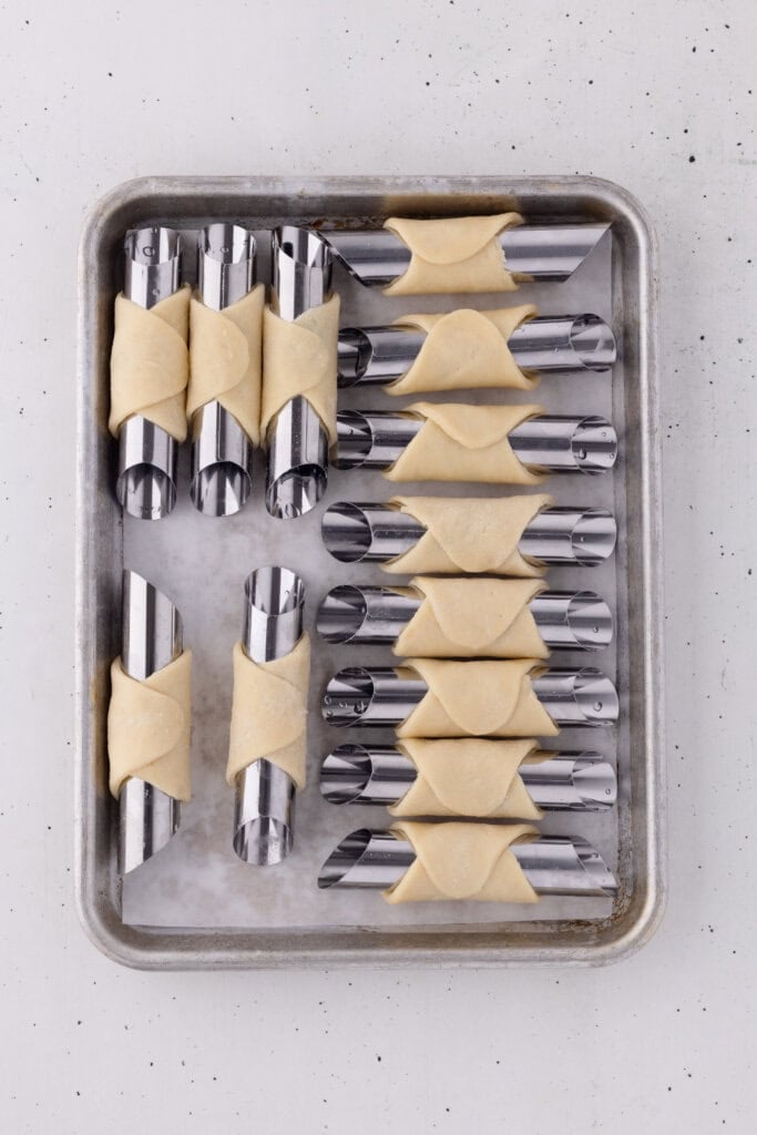cannoli dough wrapped around greased cannoli forms on baking sheet.