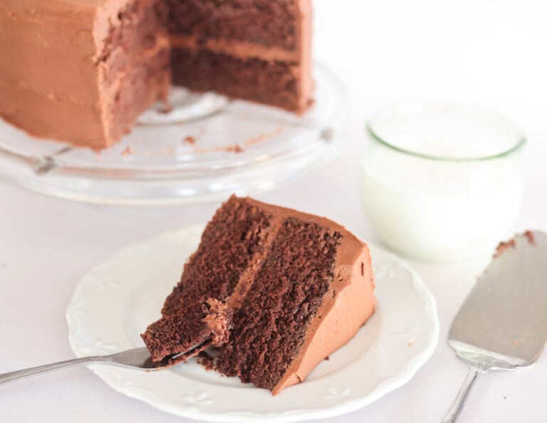 slice of sourdough chocolate cake with chocolate icing on plate with cake behind.