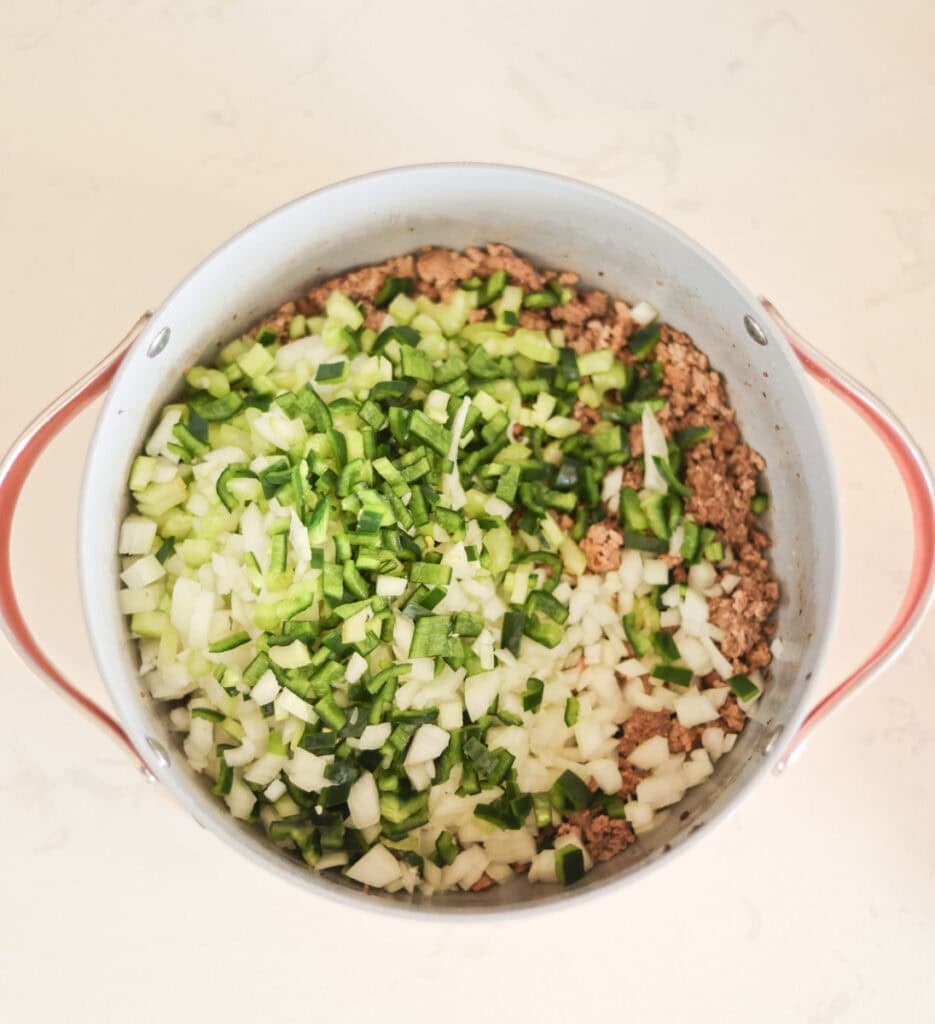 adding chopped veggies to browned meat in dutch oven.