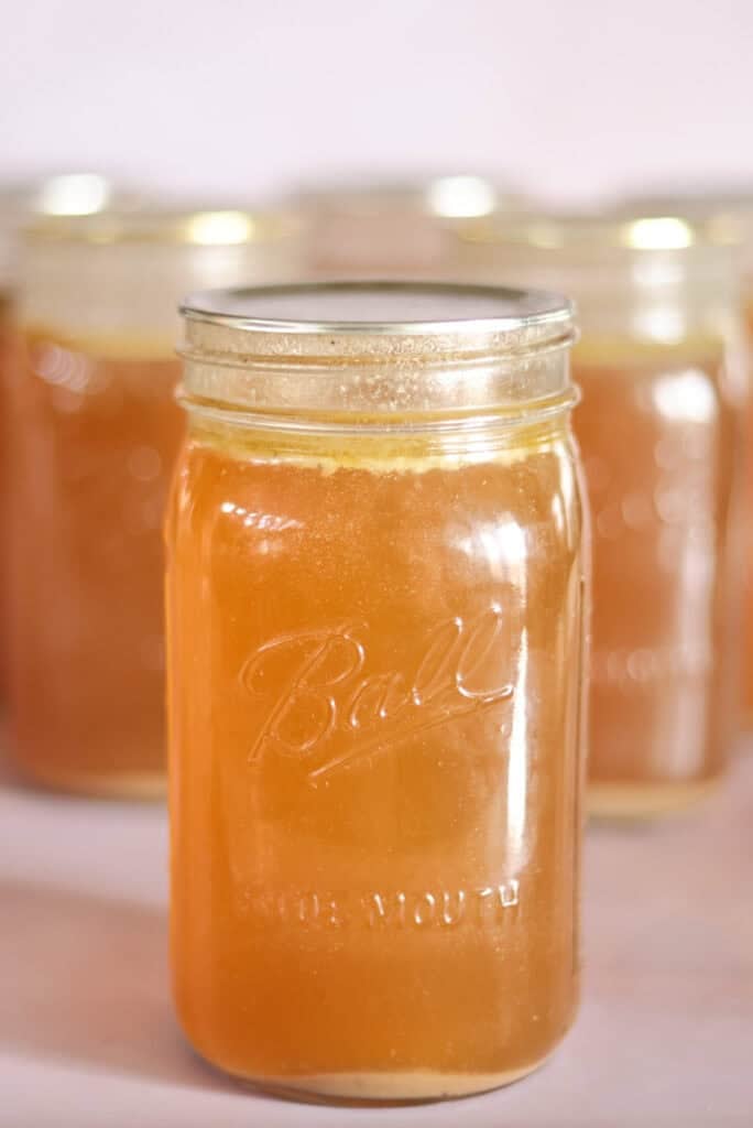 quart jar of pressure canned chicken bone broth with jars in background.