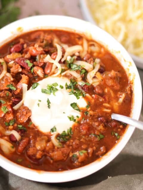 chili with dried beans in bowl with sour cream shredded cheese and cilantro.