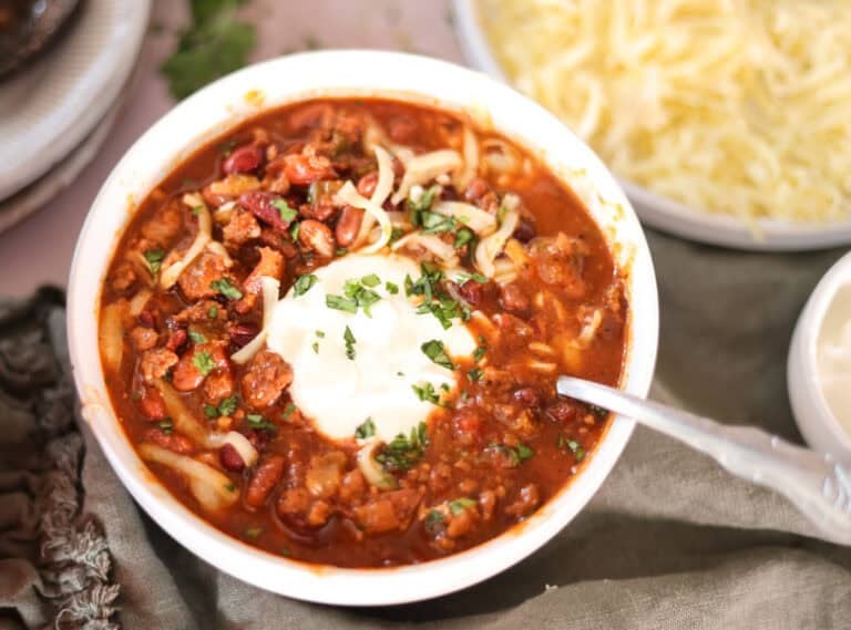 chili with dried beans in bowl with sour cream shredded cheese and cilantro.