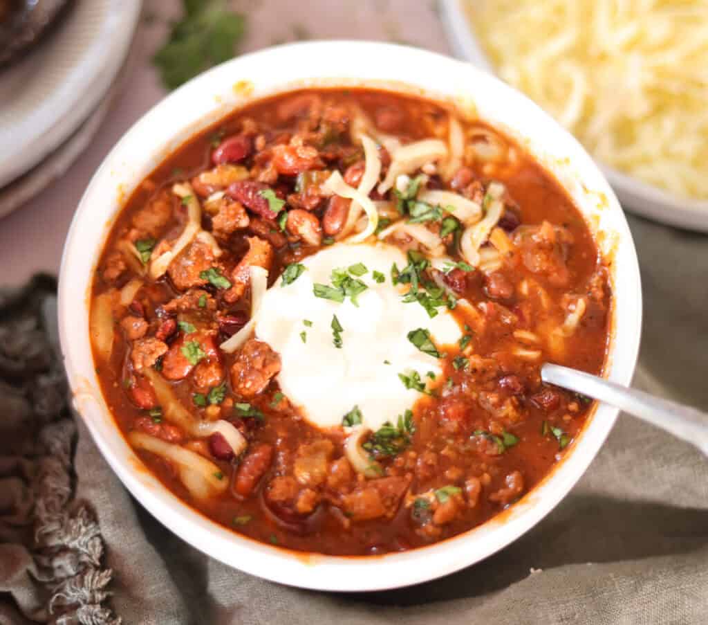 chili with dried beans in bowl with sour cream shredded cheese and cilantro.