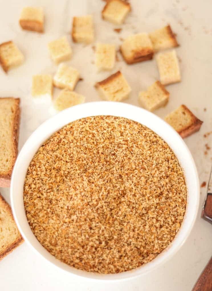 bowl of sourdough breadcrumbs with cubed bread in background.