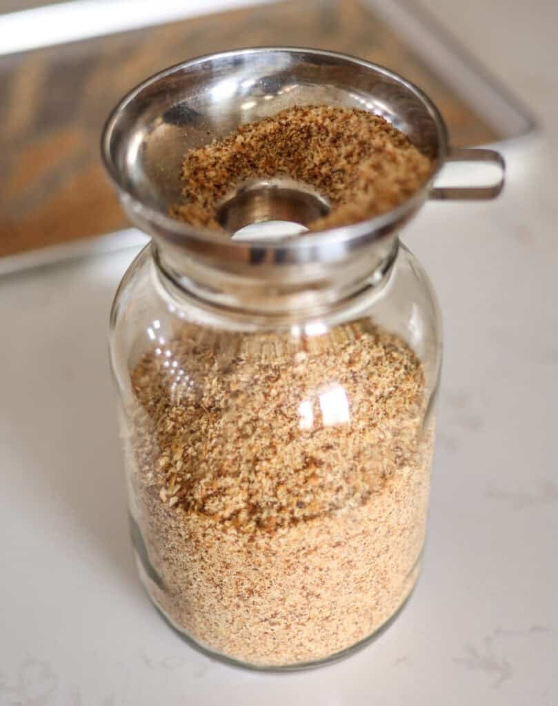 pouring cooled breadcrumbs into a jar with stainless steel funnel.