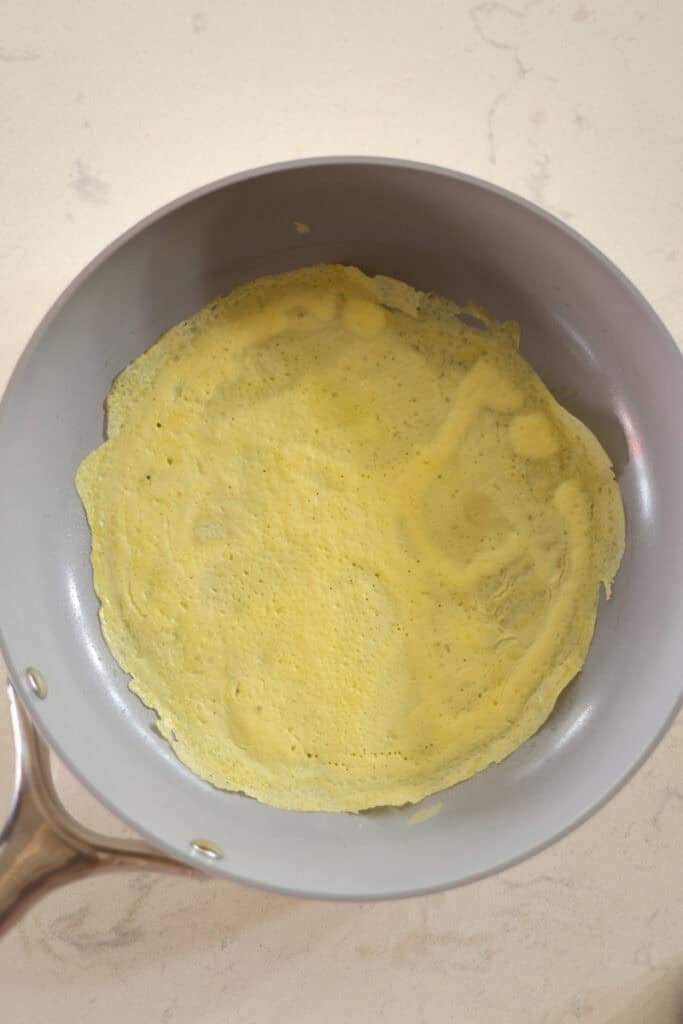 egg wrap being cooked in non stick skillet.