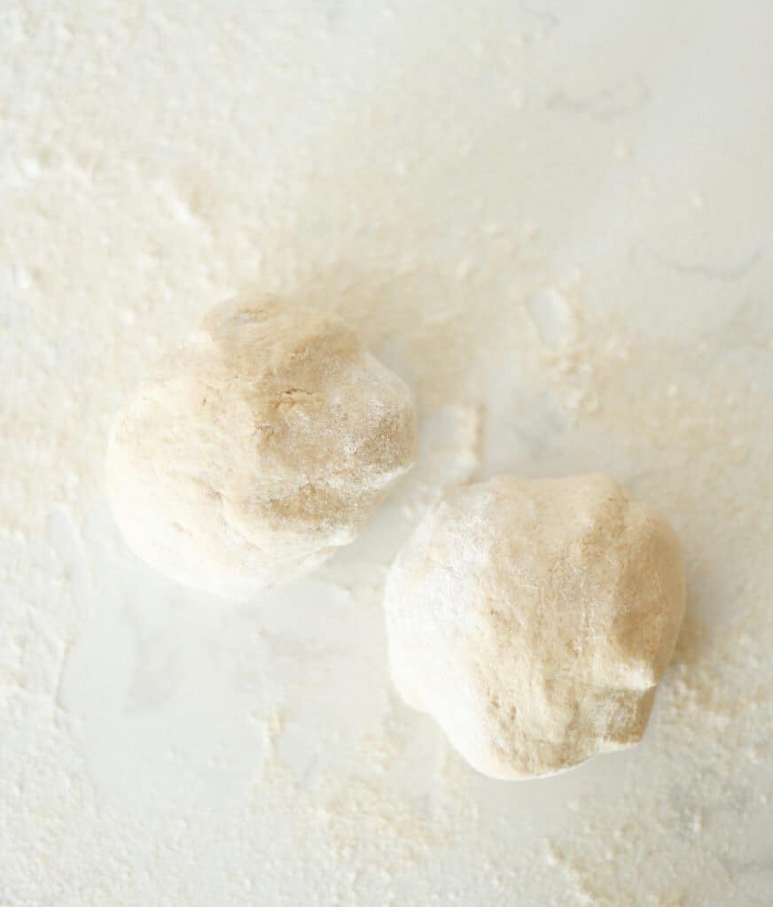 pizza dough divided into two rounds on flour surface.
