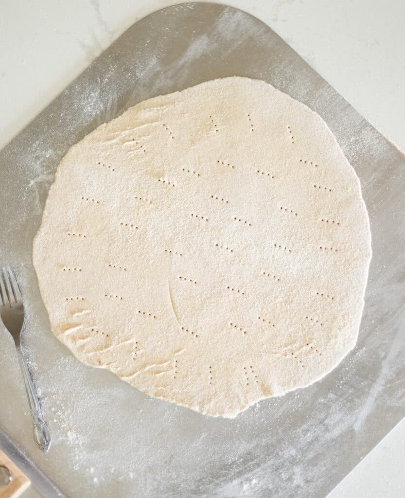 rolled out pizza dough with fork holes on pizza peel ready to bake.