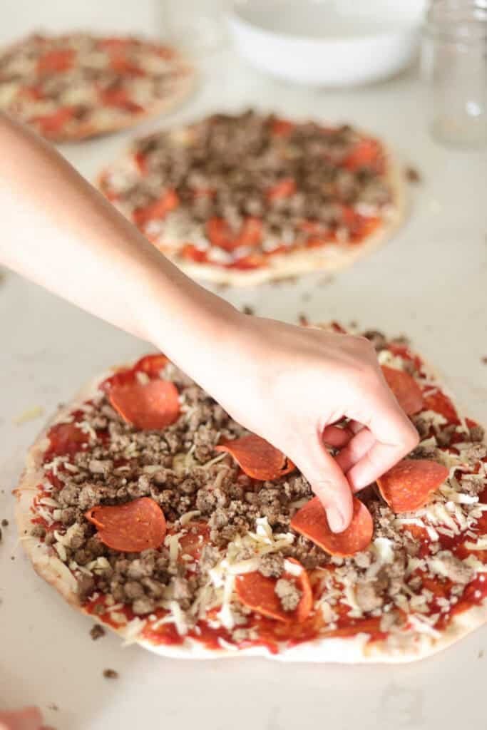 assembling pizzas with sauce cheese and toppings like pepperoni and sausage.
